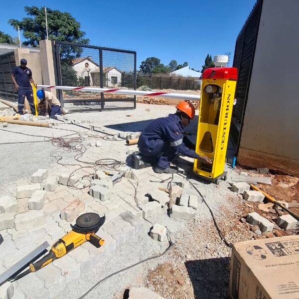 Technician in an orange hard hat installing a yellow Centurion boom barrier cabinet next to a black steel gate