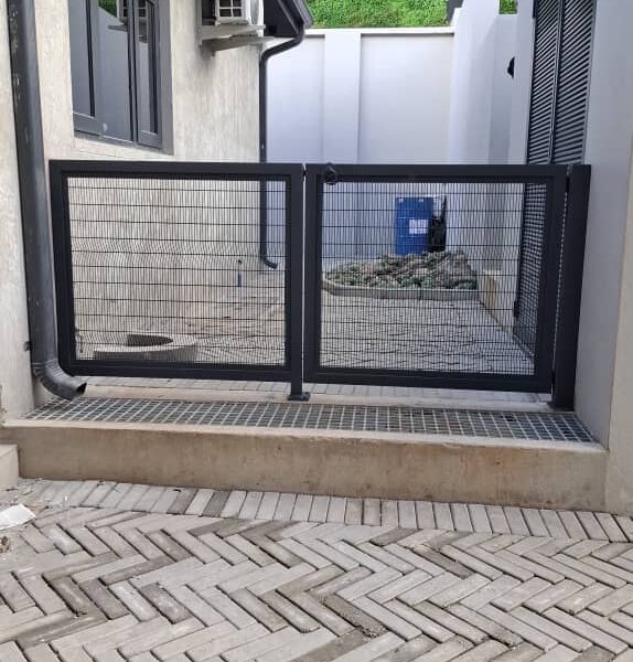 Charcoal clearview mesh double swing gate installed across a paved service courtyard entrance