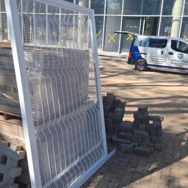 Framed white clearview mesh fence panel on site beside a branded fencing and CCTV installation van