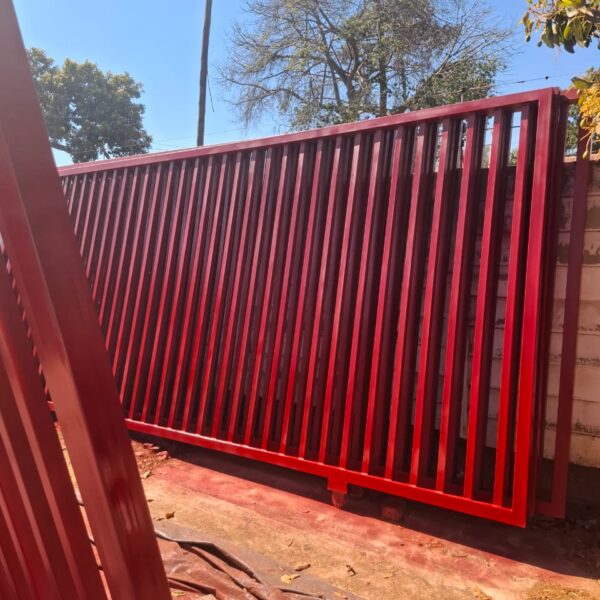 Newly painted red steel sliding gate on wheels at a boundary wall with a solar street light overhead