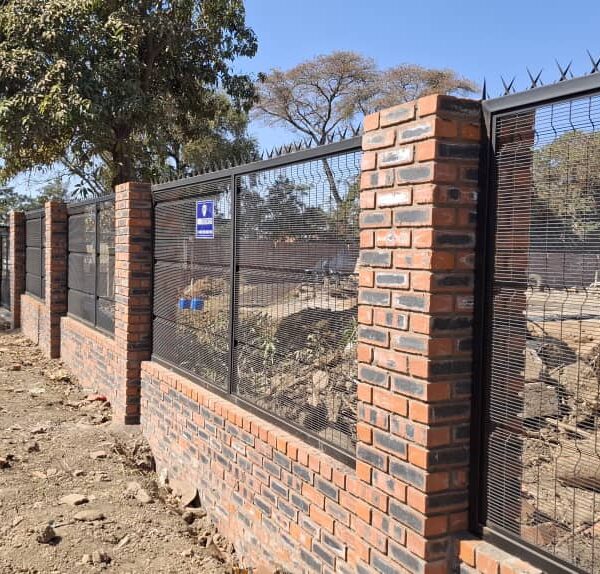 Completed black clearview anti climb mesh fencing with spiked top on the face brick plinth wall, Kadoma