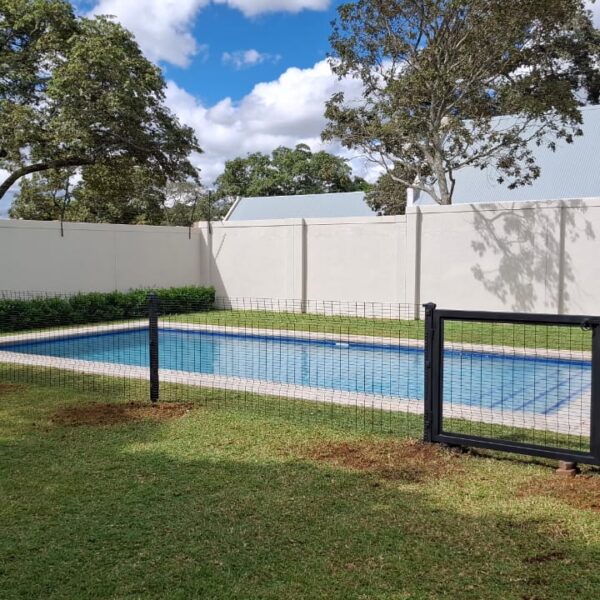 Black welded mesh pool safety fence and framed pool gate around a swimming pool on a lawn in Greendale