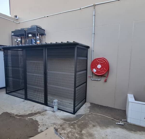 Completed black steel refuse enclosure with clearview mesh panels and sloped roof in a commercial service yard