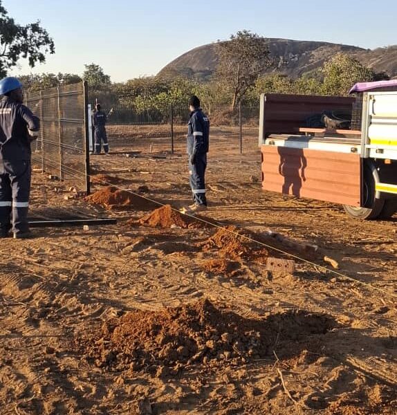 Fencing crew erecting welded mesh panels beside a truck on a rural perimeter fence line