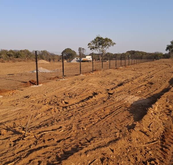 Completed run of dark welded mesh perimeter fencing along a cleared strip in open bush country