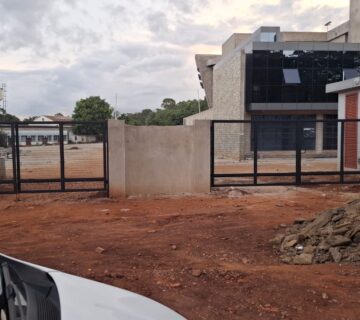 Black steel swing gates with welded mesh infill at the vehicle entrance of a modern office complex